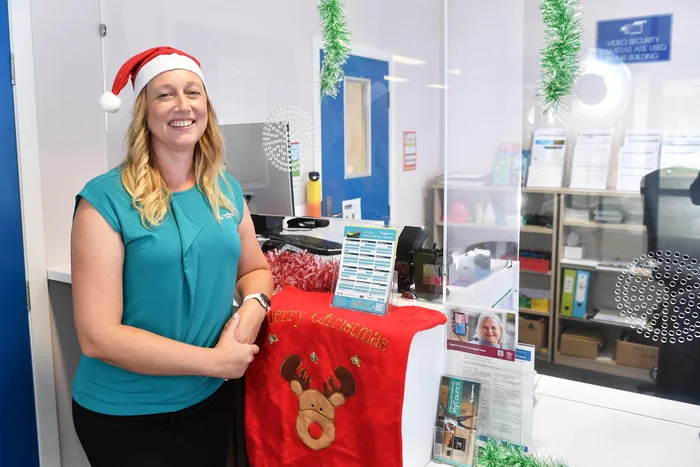 A woman wearing a Santa's hat and a Council uniform leans against a customer service counter that has Christmas decorations on it.