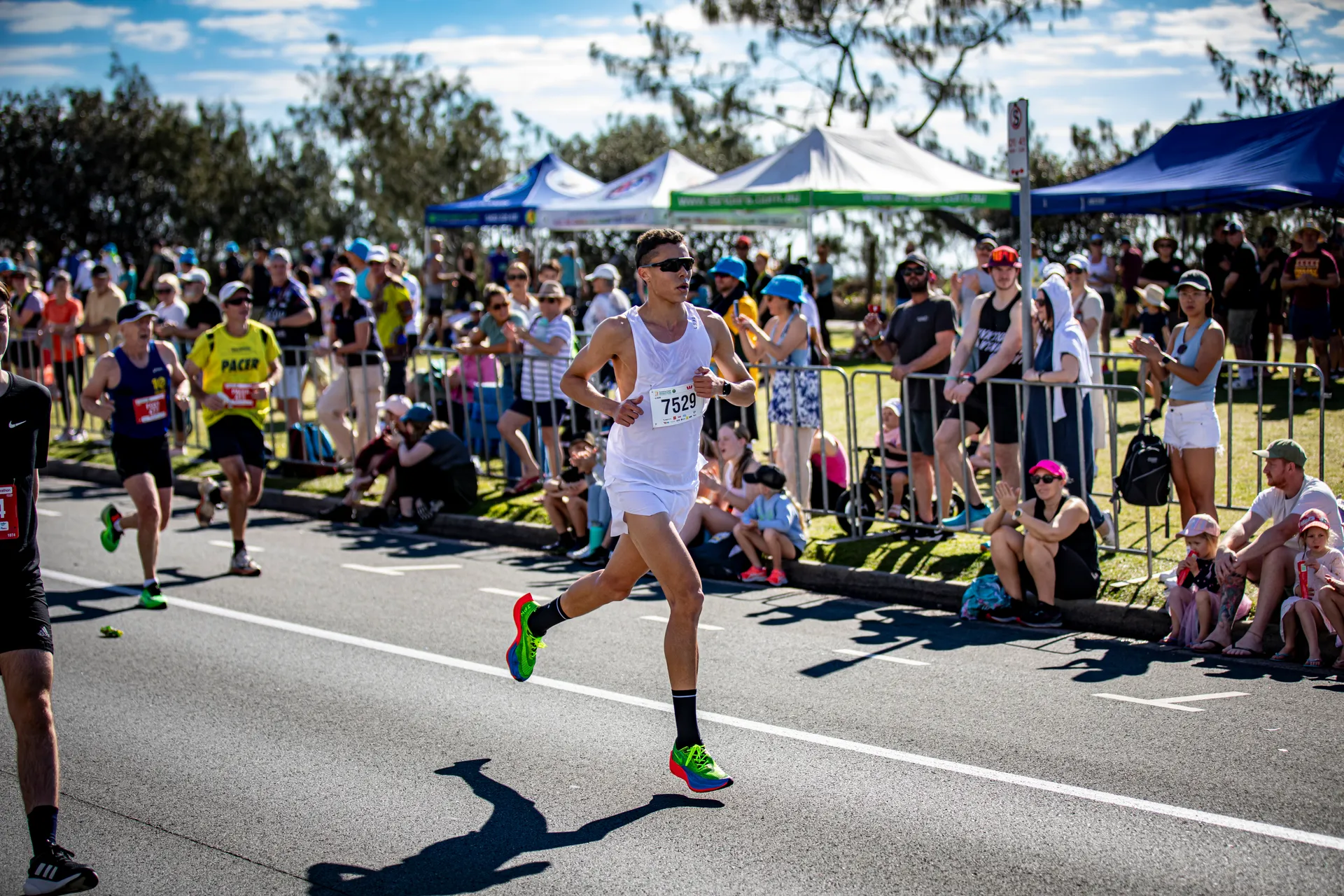 A marathon runner on the road in the foreground, and spectators lining the fence on the sideline