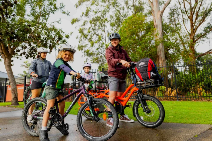 A schoolboy with his mum, dad and little sister are all stationary on bicycles, all wearing helmets.