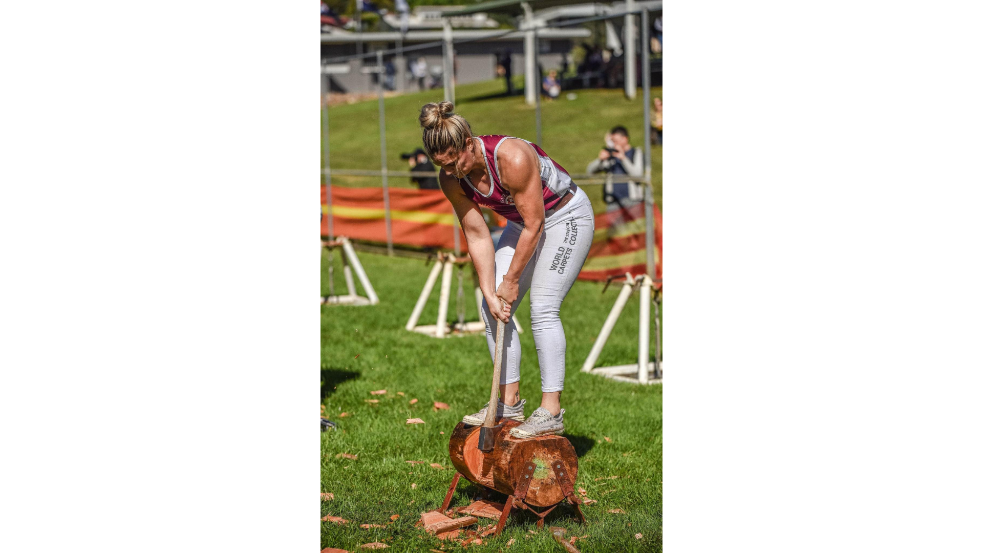 Chopping wood - a lady standing on a wood log bending over it with her axe chopping into the log.