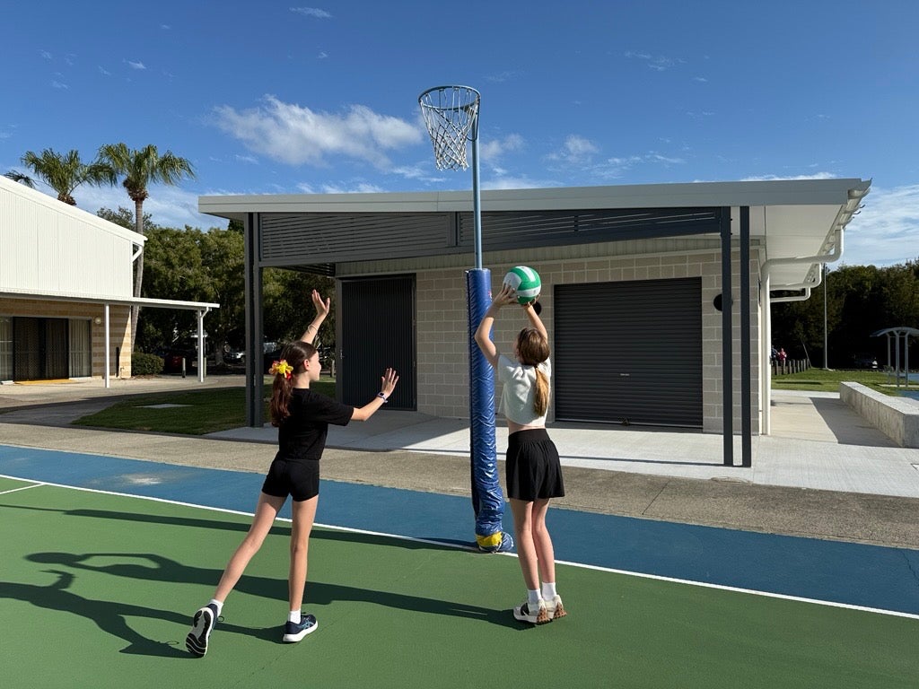 Young girls playing netball, with new Play Our Way amenities in the background, Caloundra Indoor Sports Complex