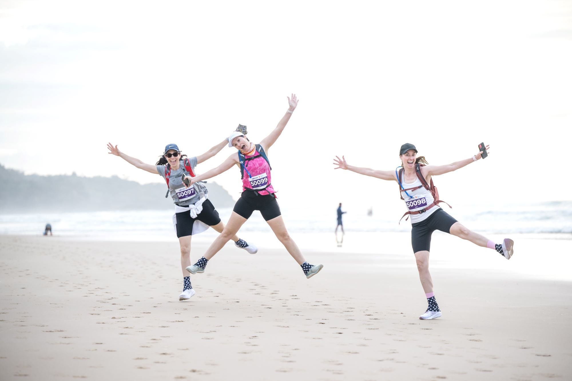 On the beach/sand, three people jumping like starfish - walkers in Coastrek fundraising event