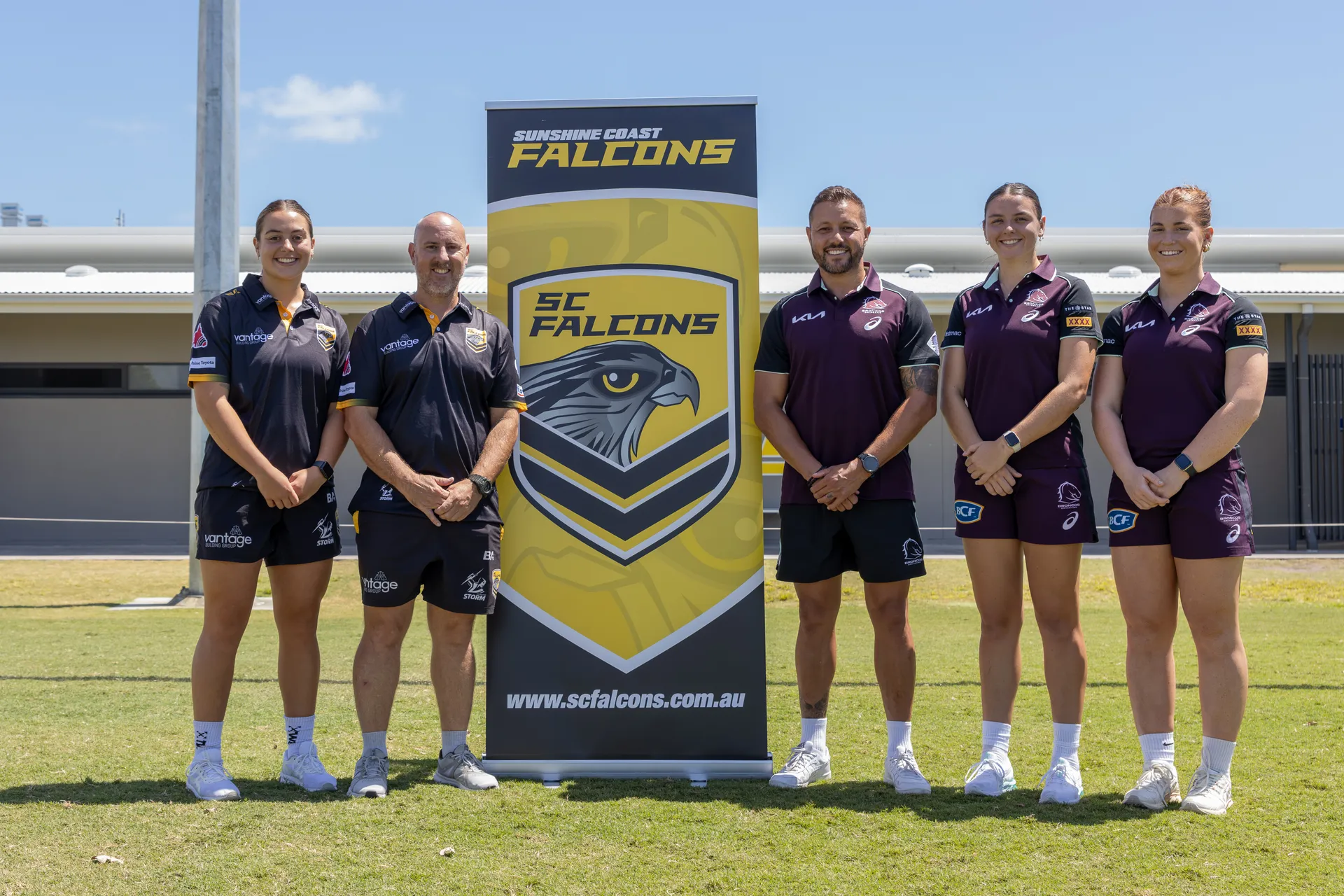 A group of 5 people from Falcons and Broncos club standing beside Falcon's branded signage.