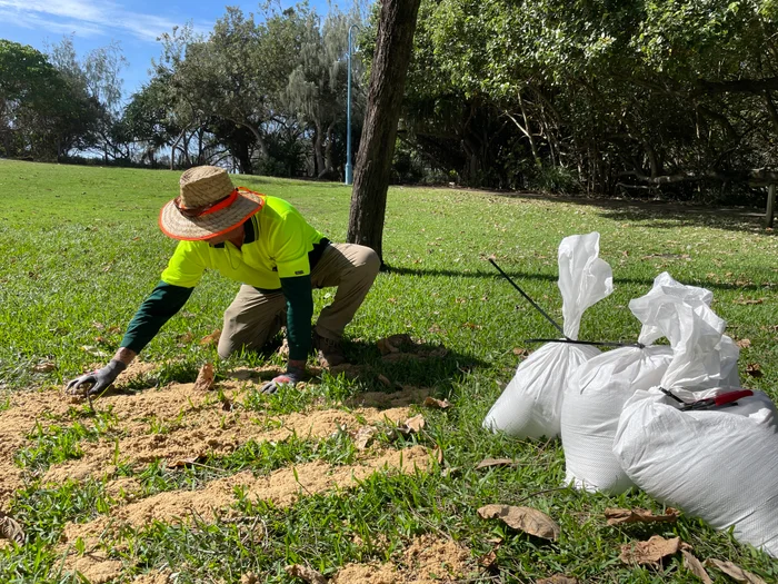 A Council worker spreads sand from used sandbags across grass as a top dressing.