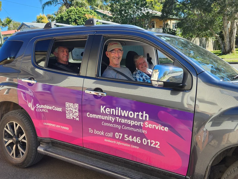 A Kenilworth Community Transport Service car, covered in Sunshine Coast Council branding with a group of people inside. They are smiling and looking out the windows.