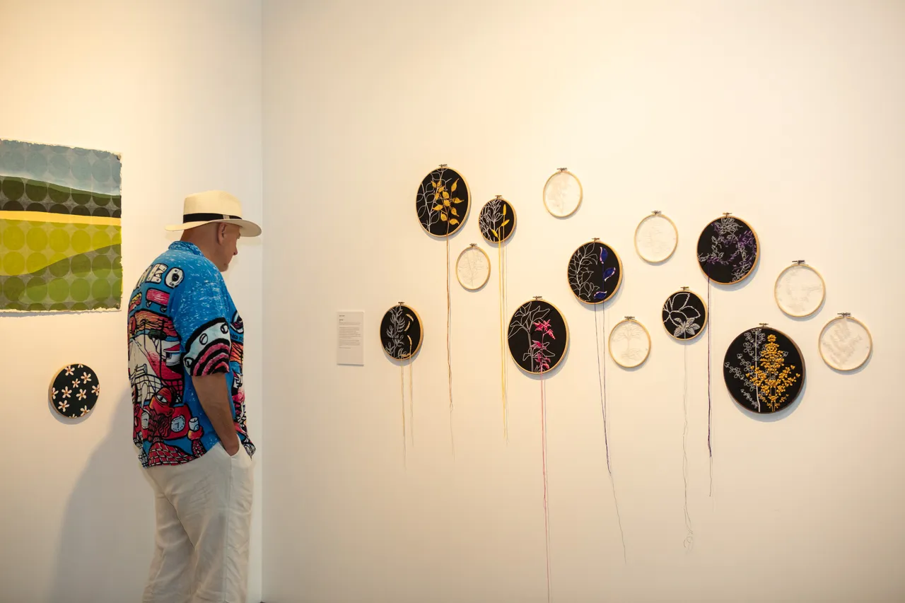 A man in a hat standing in front of a range of artworks at the Wildflowering by Design exhibition launch