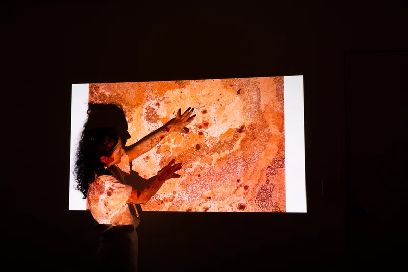 An artist holding her hands up across a projected screen work
