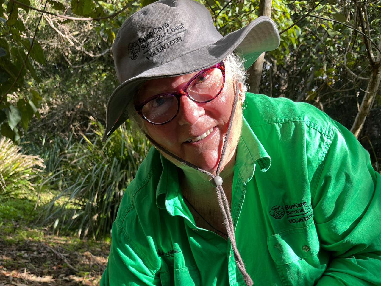 Woman wearing BushCare volunteer uniform stares into camera.