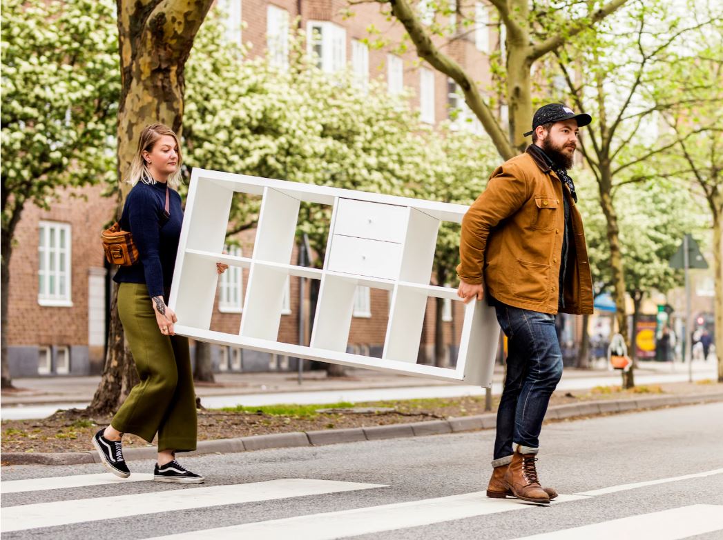 couple carrying a cabinet across a road