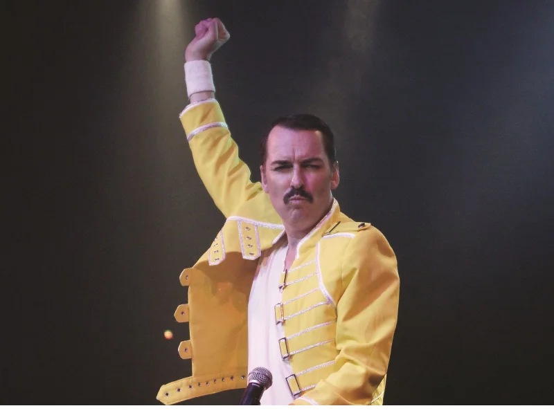 Queen Bohemian Rhapsody tribute band. Impersonator Thomas Crane dressed in signature yellow buckle jacket. Personifying Freddie Mercury's energy and signature pose of one arm punching to the sky.