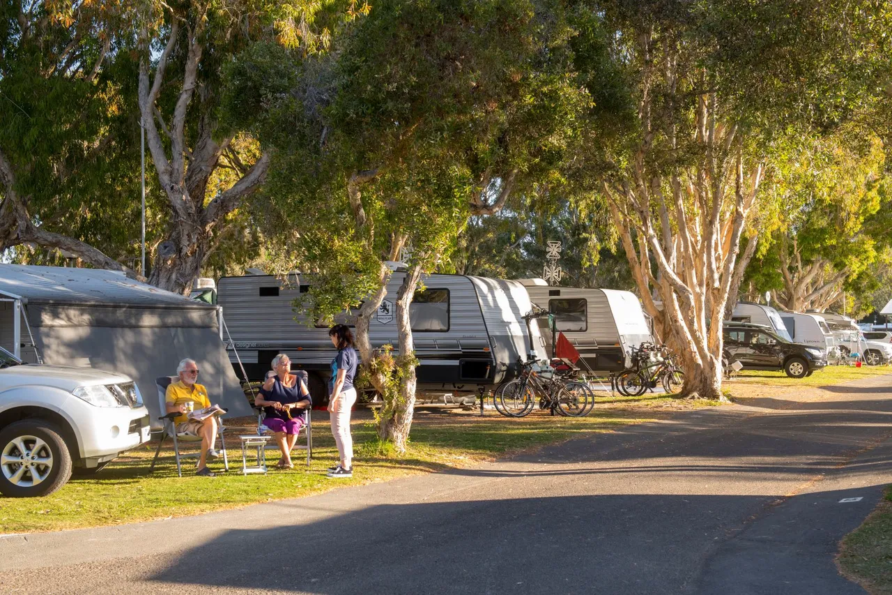 People sitting next to caravan at Mudjimba Beach holiday park near tall trees