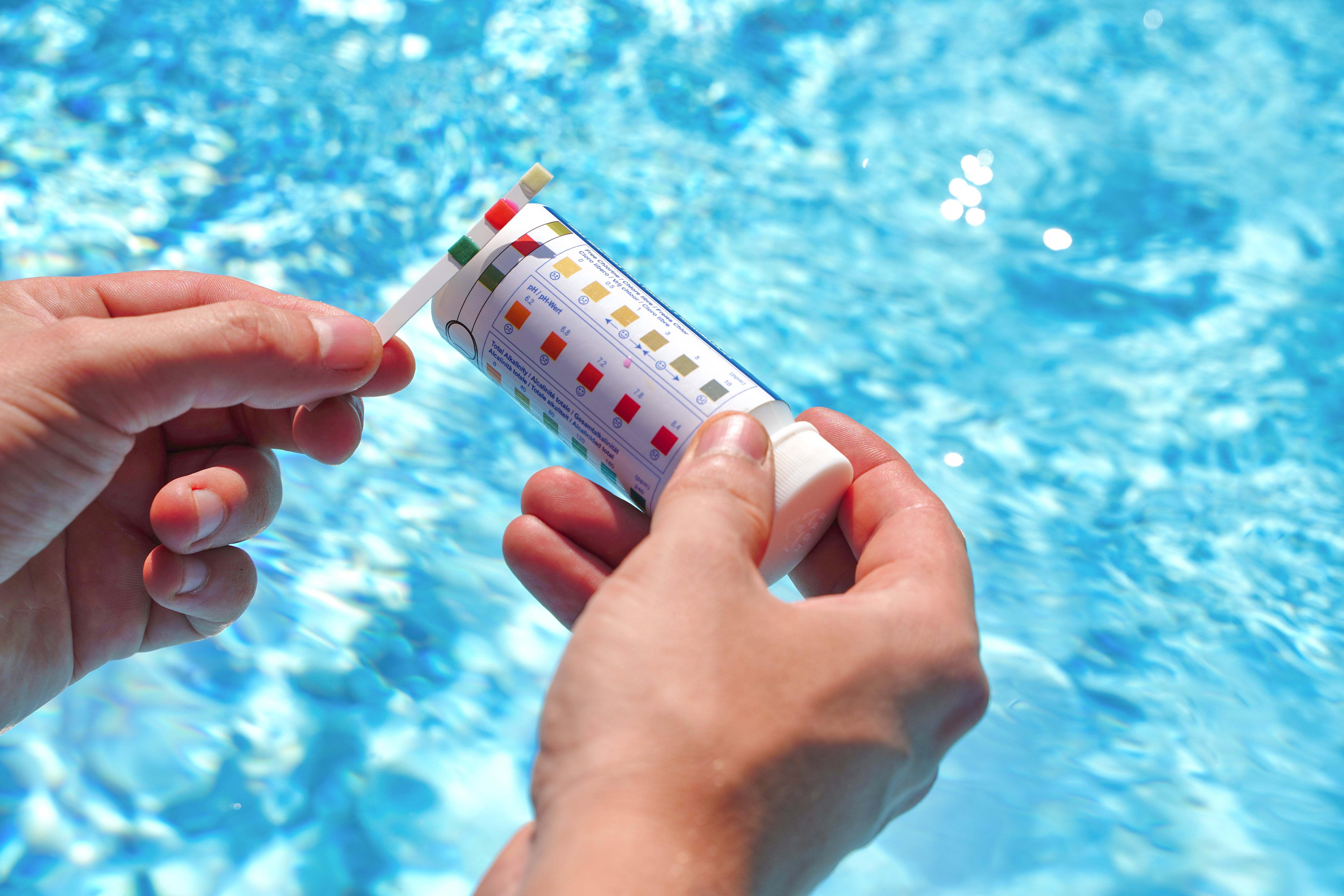hands holding DIY pool test strips, comparing colours above a pool