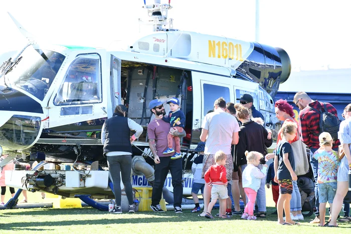 A line of happy, young family's wait to sit in a stationary helicopter in a field.