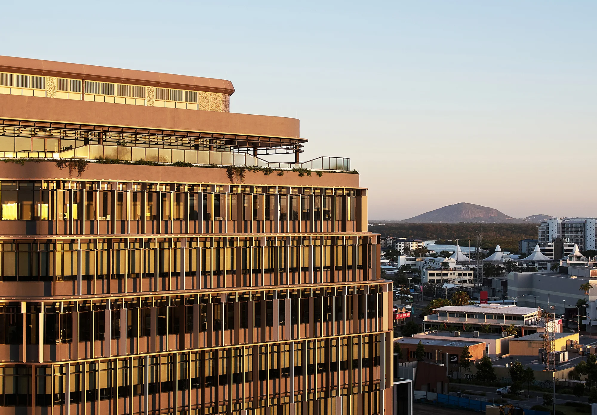 Aerial shot of a building with a rooftop bar in the sunset with mountains in the background