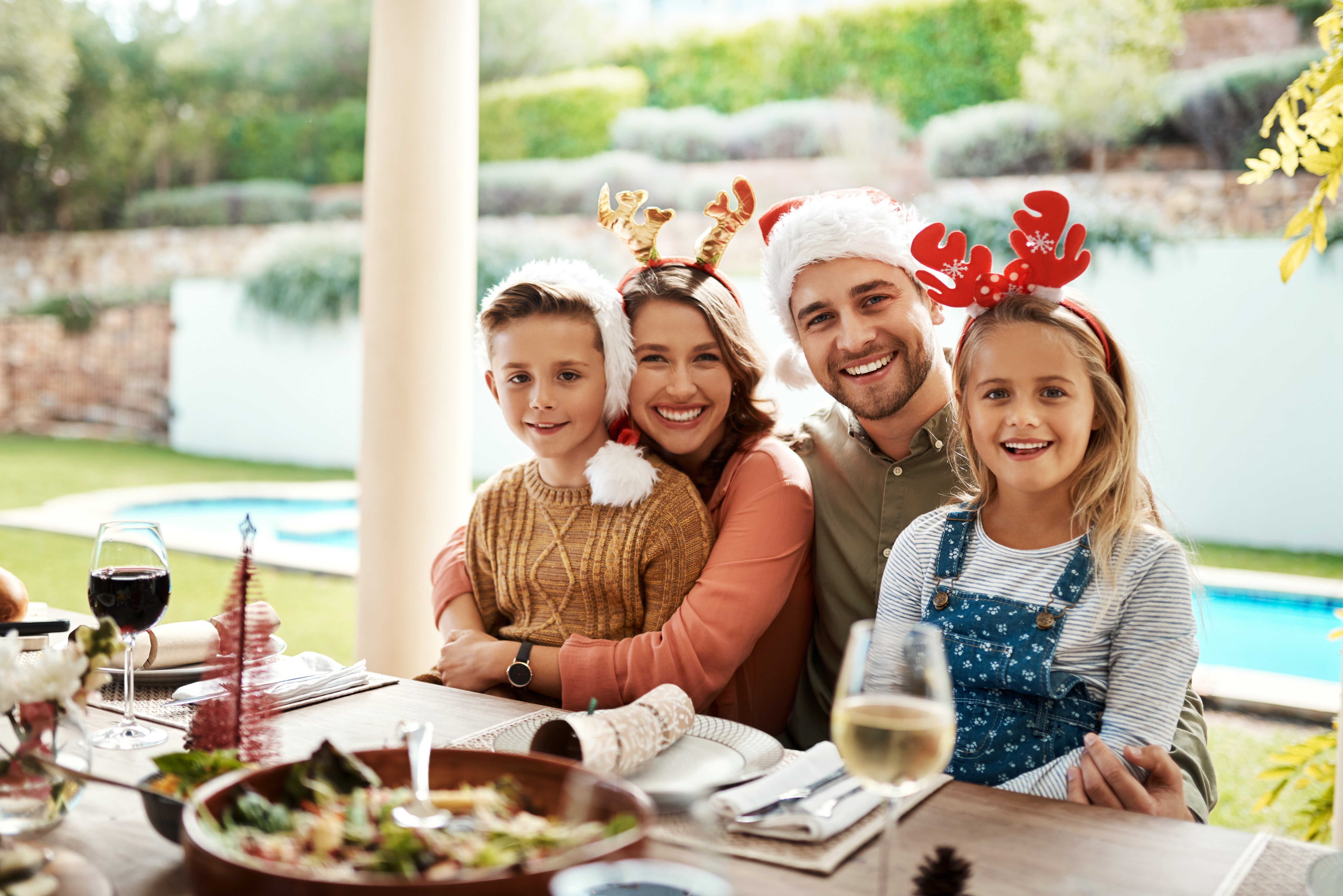family sitting around a table at Christmas with a pool behind them