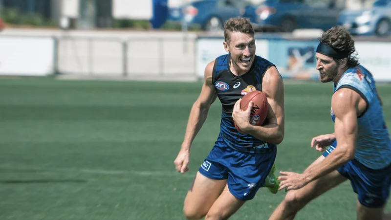 Image of two AFL players, one holding the ball under his arm.