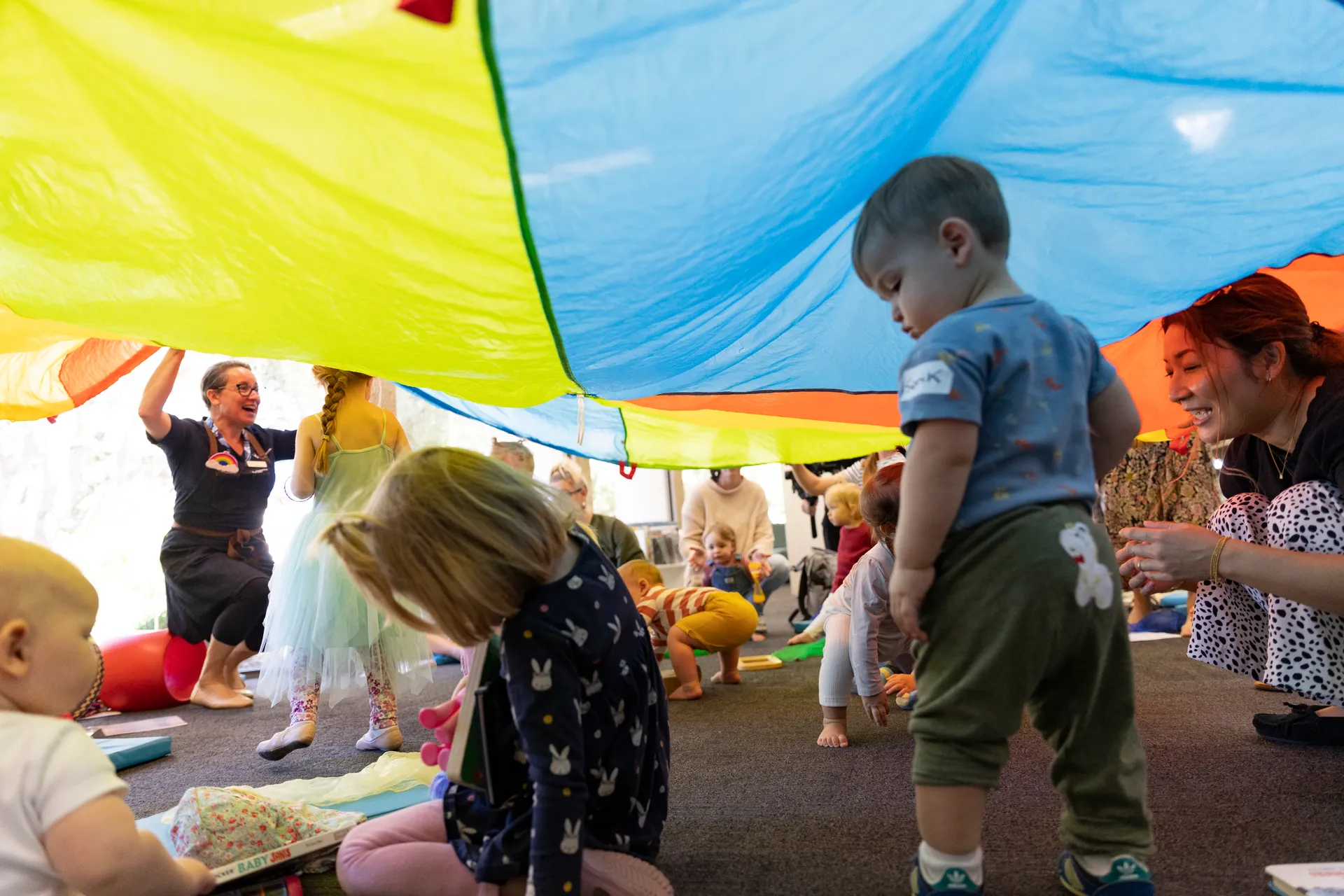 Sunshine Coast Libraries Storytime session with kids aged 2 to 5 years old playing under a colourful parachute.