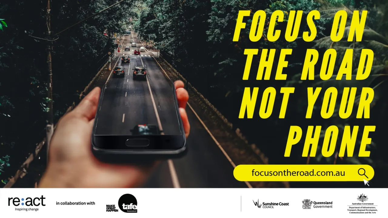 Bright yellow words 'Focus on the road not your phone' campaign. Images show a large hand holding a black mobile phone over a road with cars driving from it.