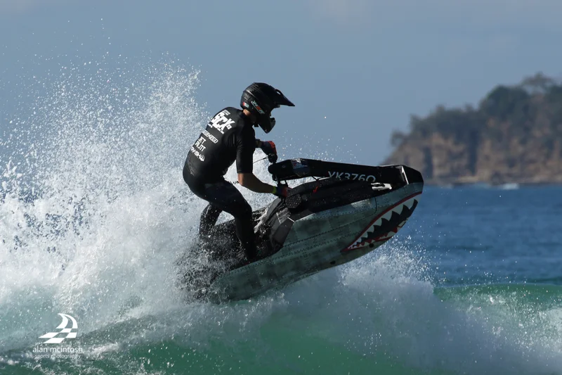 Jet Ski rider scooting up a wave, with ocean spray coming off the back