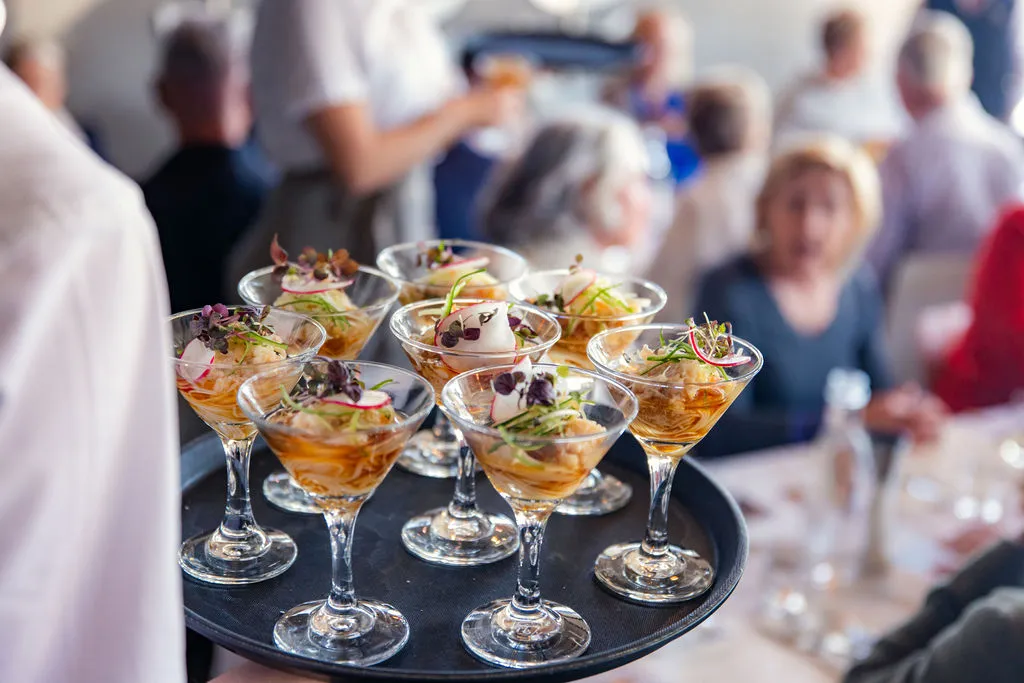The Curated Plate - a tray of glasses filled with food and blurred background of people seated at tables