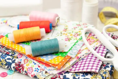 A pile of fabric samples with some coloured thread on top