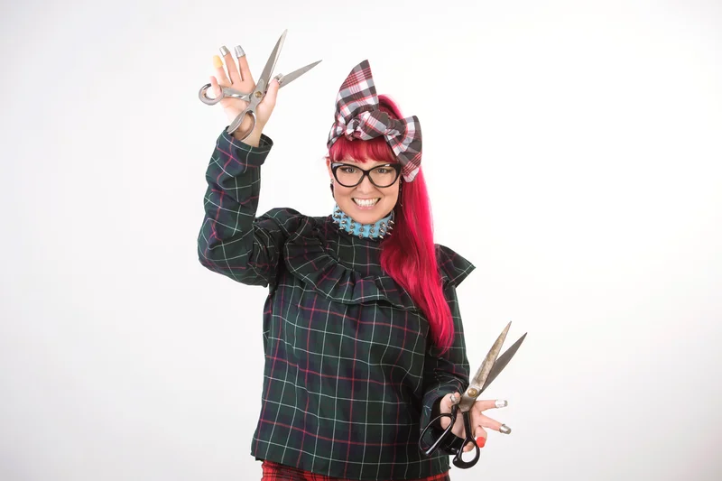 Fashion designer Cindy Vogels wearing a big bow in her and holding a pair of scissors in each hand.