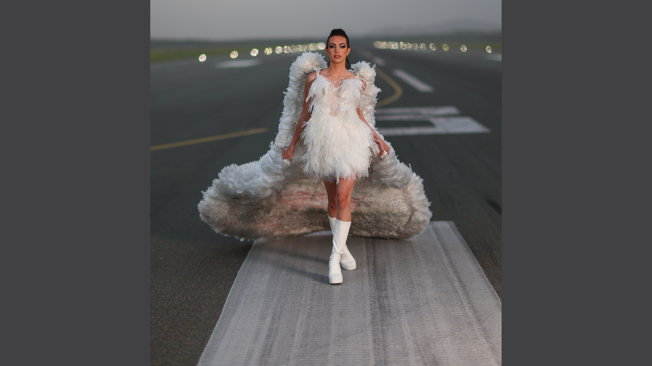 Model Jodi Urli wears Plastic Rain by Natalie Hamblin (2024 Runner-up Trashion). Jodi is standing on the Sunshine Coast Airport runway, with runway lights in the distant background.