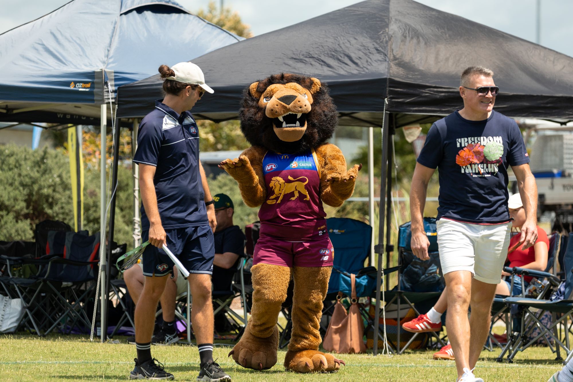 A helper guiding the Brisbane Lions mascot, with a another person in the picture that just happens to be walking past.