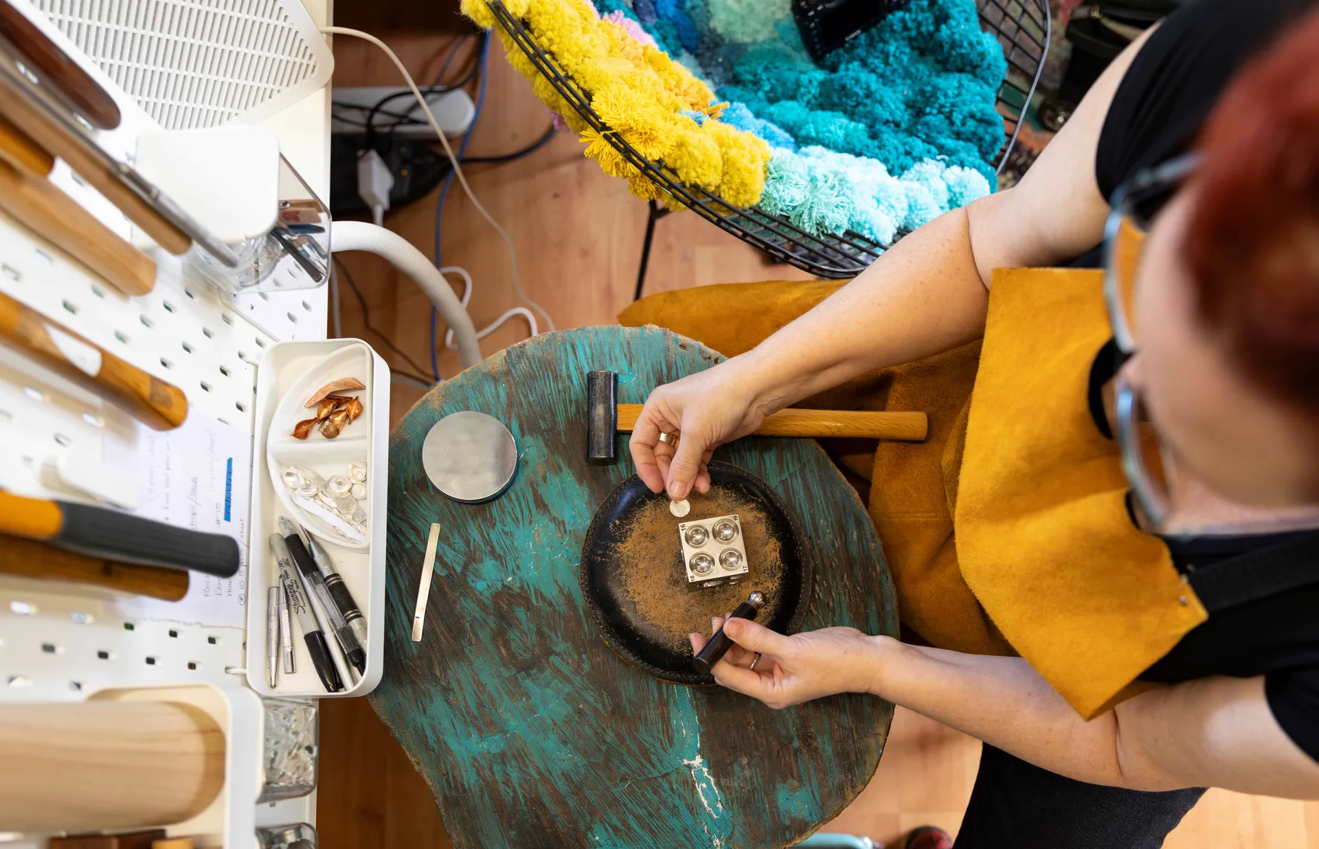 Looking down over a woman with red hair, wearing an apron making jewelry.