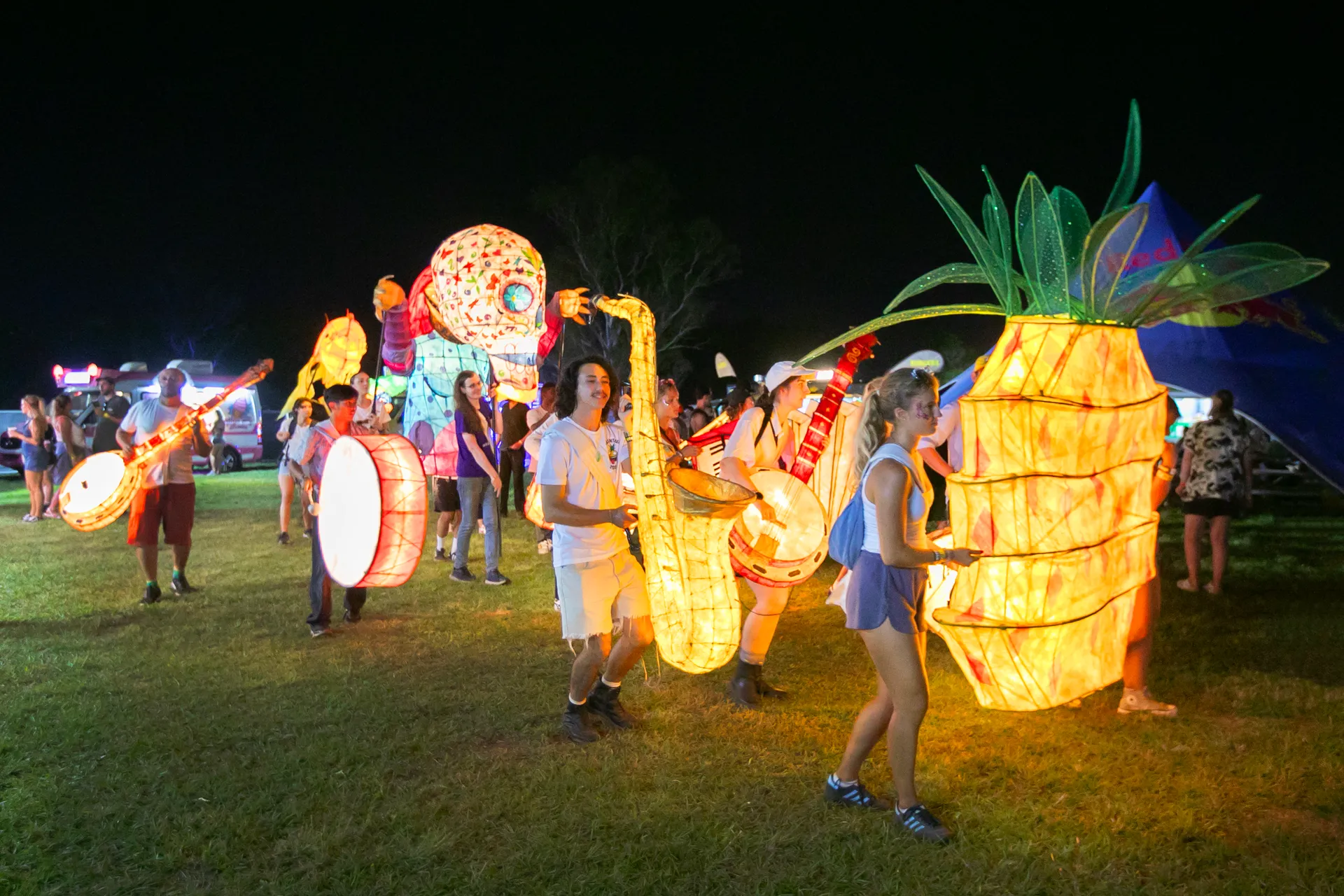A number people holding 'lanterns' shaped like a pineapple, saxophone, banjo, skull, drum, and guitar
