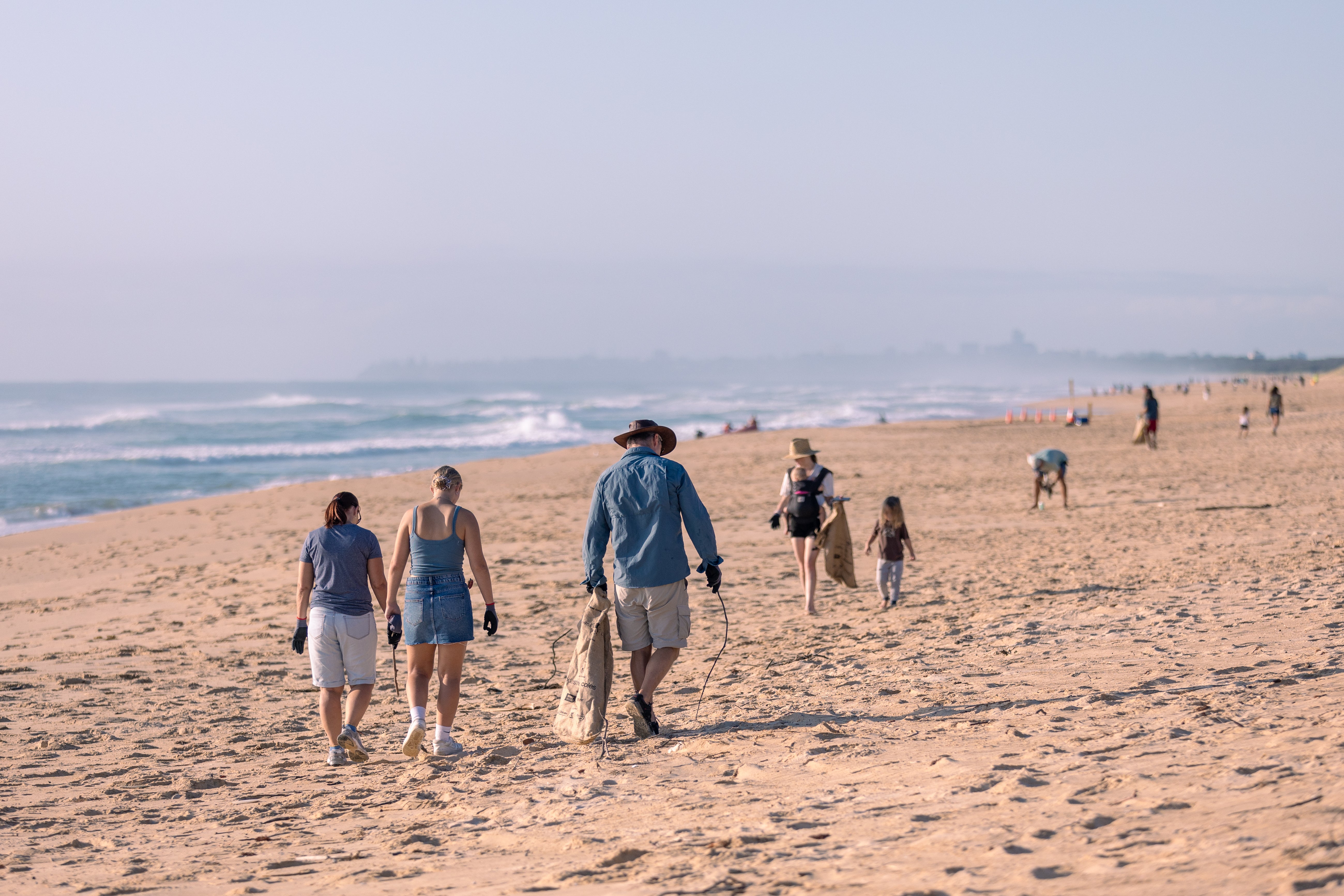 A group of people walking along the sandy beach collecting rubbish, working together to clean up the environment.