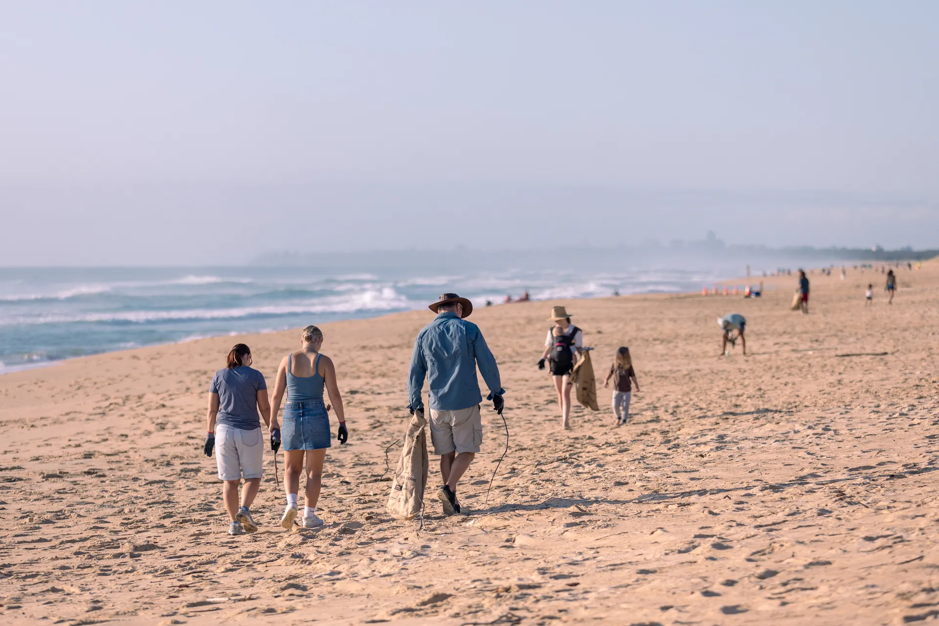A group of people walking along the sandy beach collecting rubbish, working together to clean up the environment.