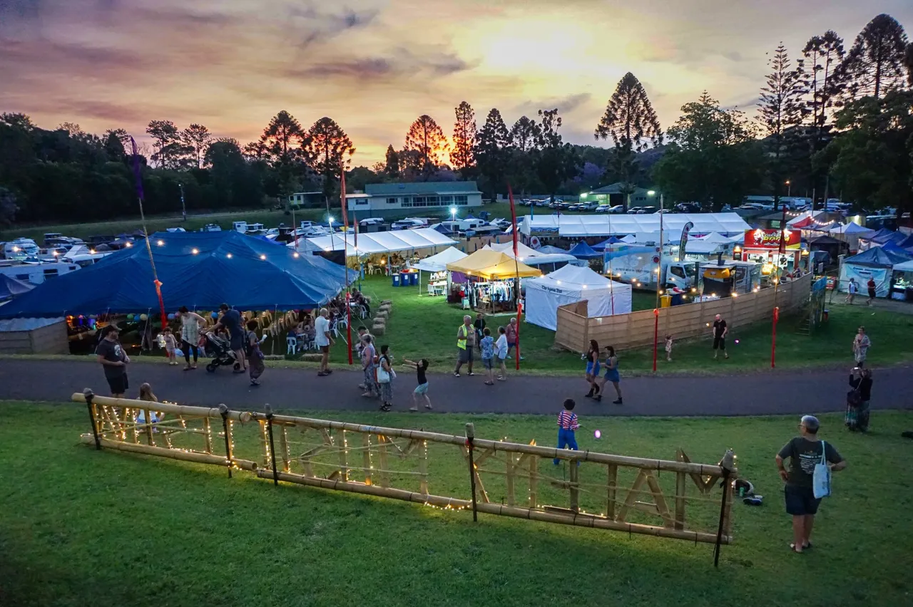 The view of the Maleny Festival at dusk. Tents covered in fairy lights with tall trees in the background.