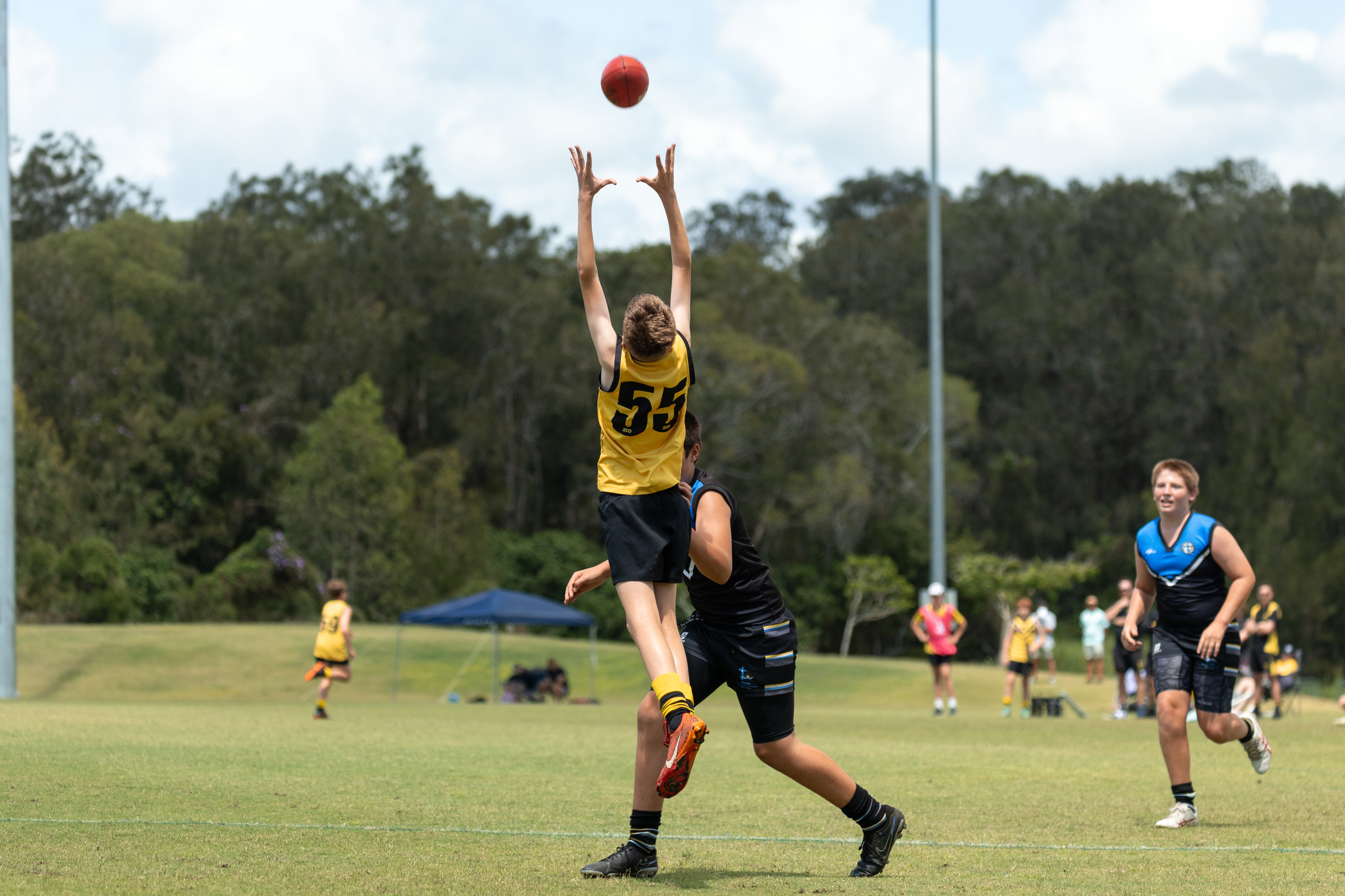 A young AFL player jumping for the ball.