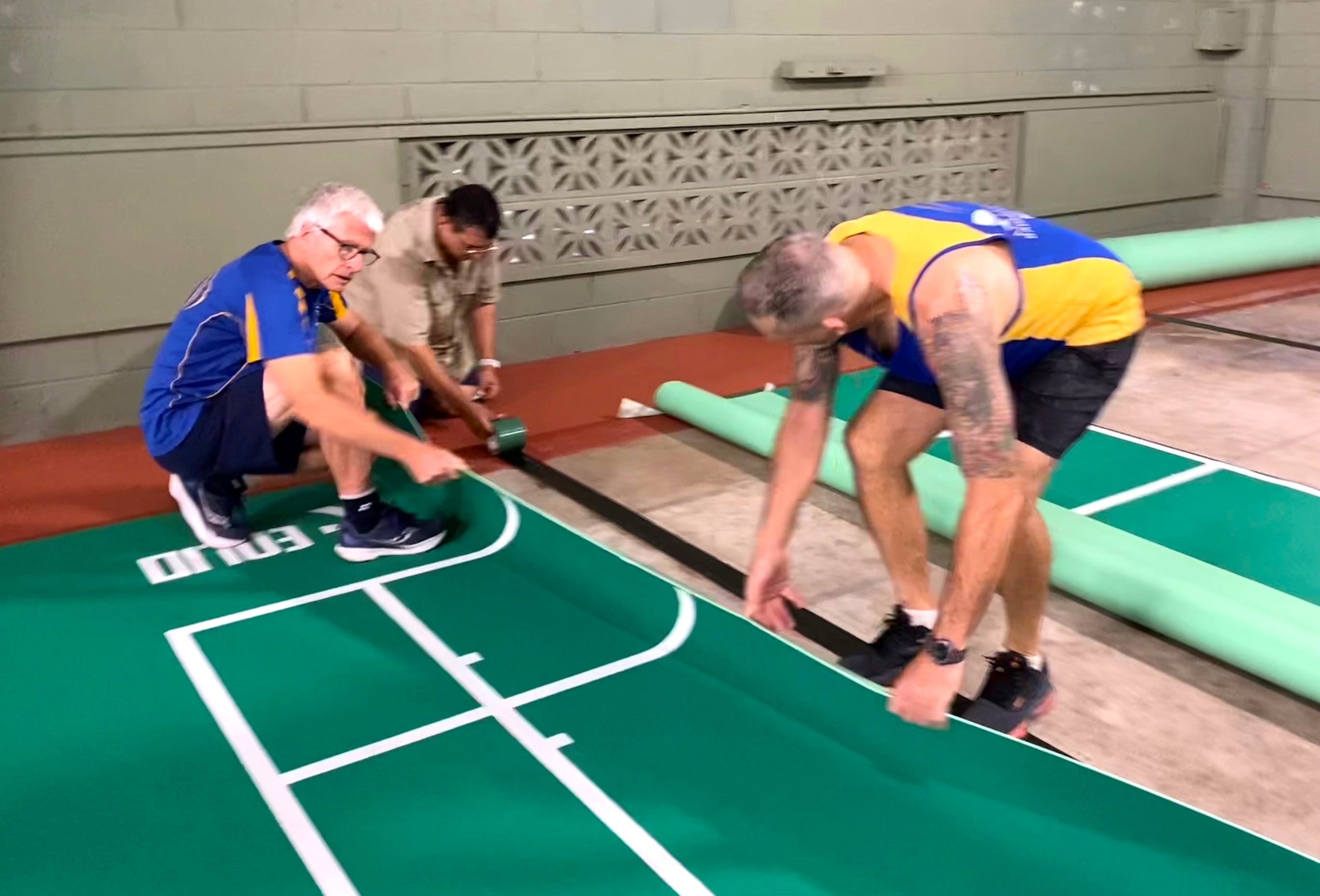 Three men are fixing the badminton court surface.