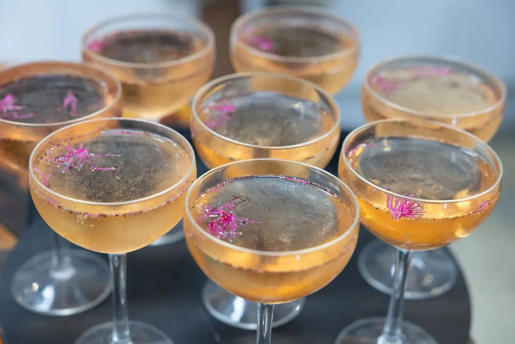 A tray of 8 cocktail glasses, with a tiny pink flower garnish