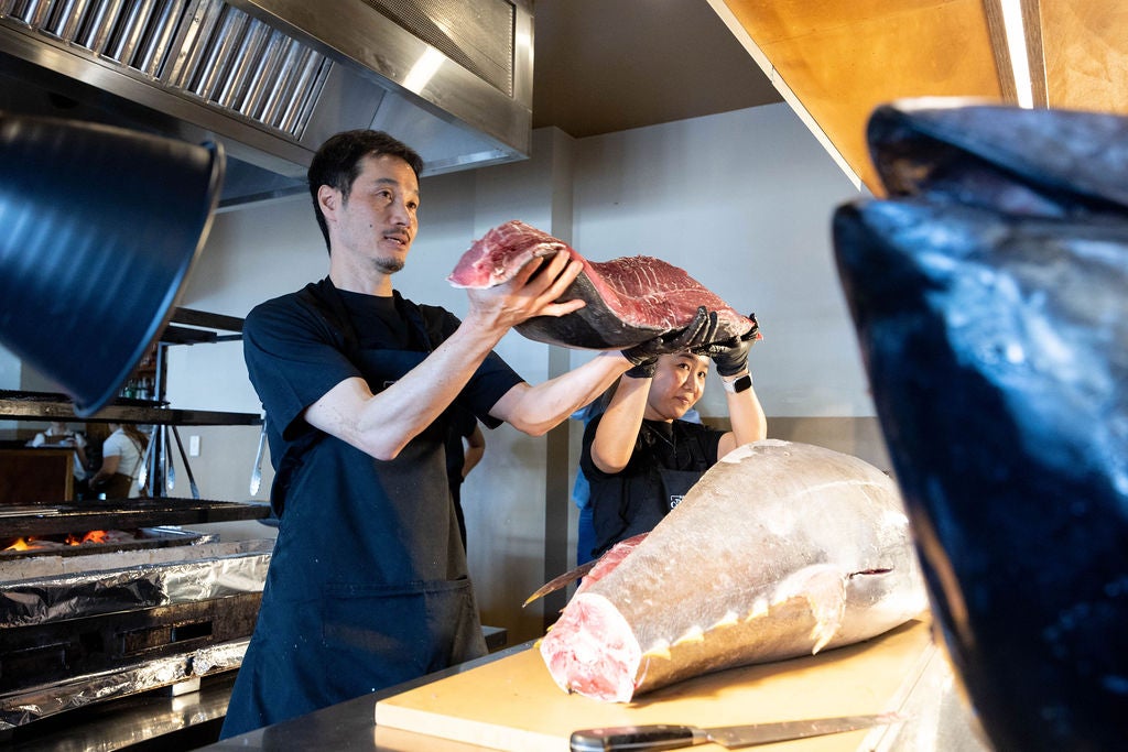 Chef from SOKA Restaurant holding up a piece of sliced tuna, with the main tuna body still on the table.