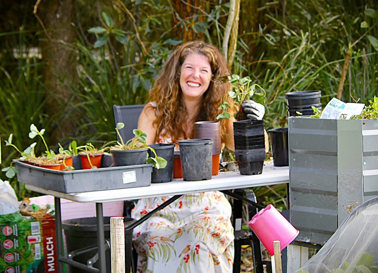 A smiling volunteer sits behind a table potting seedlings.