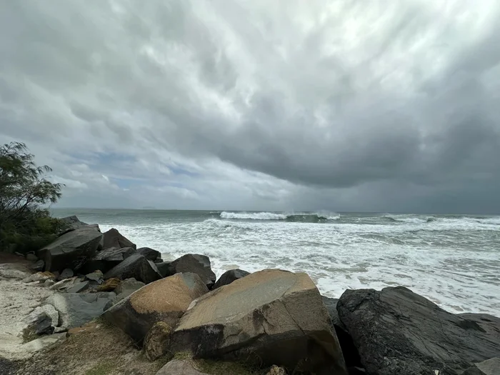 Storm clouds loom over rough ocean waves with rocks in the forground.