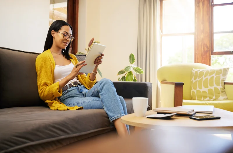 A women sits on a couch in her living room while reading an e-magazine on her iPad. 