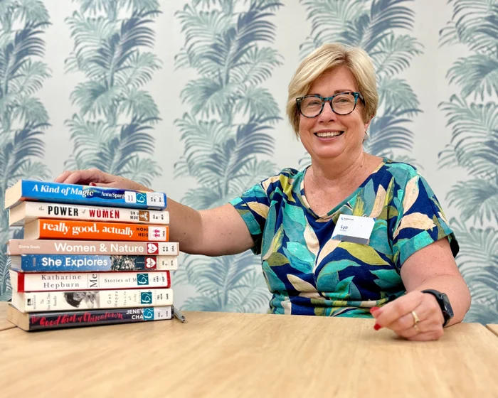 Volunteer Lyn Gavin sits with her hand on a stack of books. 