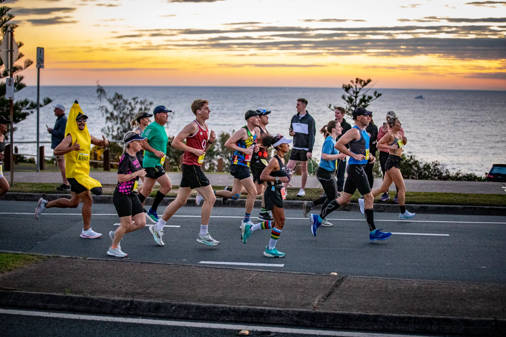 Group of runners on the road in the foreground, with the stunning morning sunrise and ocean in the background.