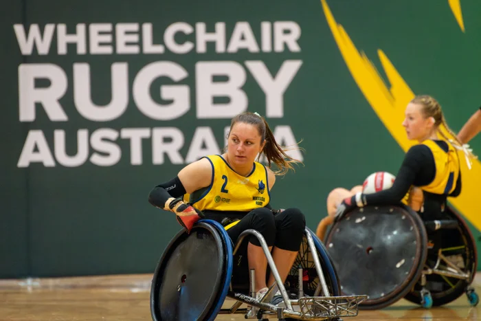 Two parasport athletes in wheelchairs wearing yellow bibs, in front of a sign that reads Wheelchair Rugby Australia