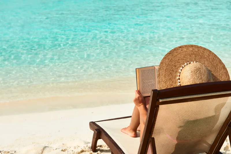 Women reading a book on a brown sheer chair by the beach and calm sea.