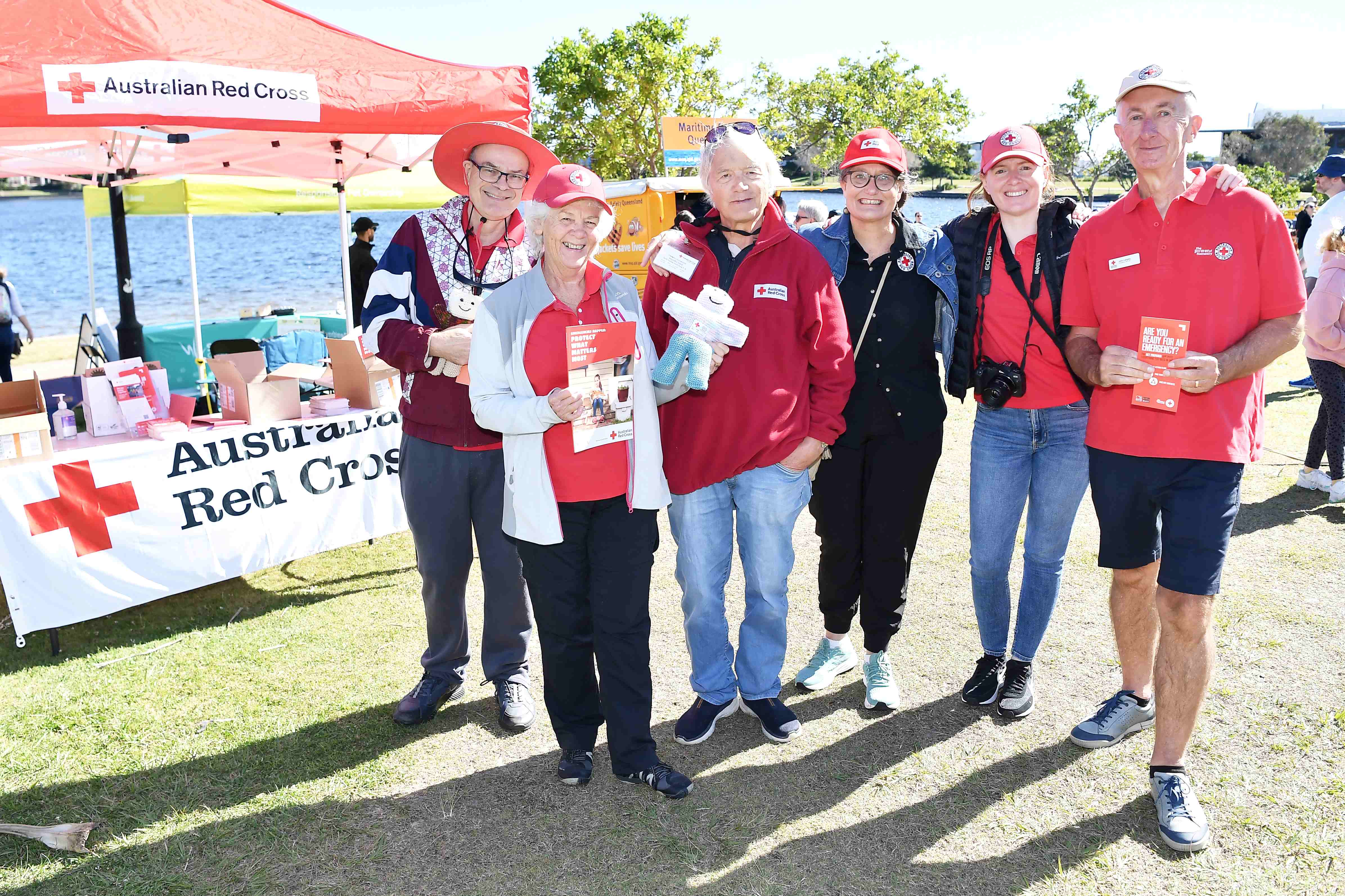 Six smiling Red Cross volunteers stand in front of the Red Cross stall.