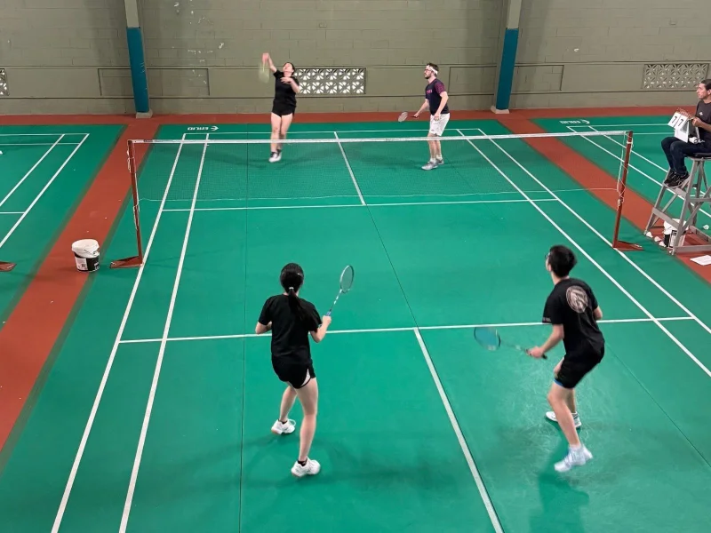 Two men and two women are playing badminton on a green court.