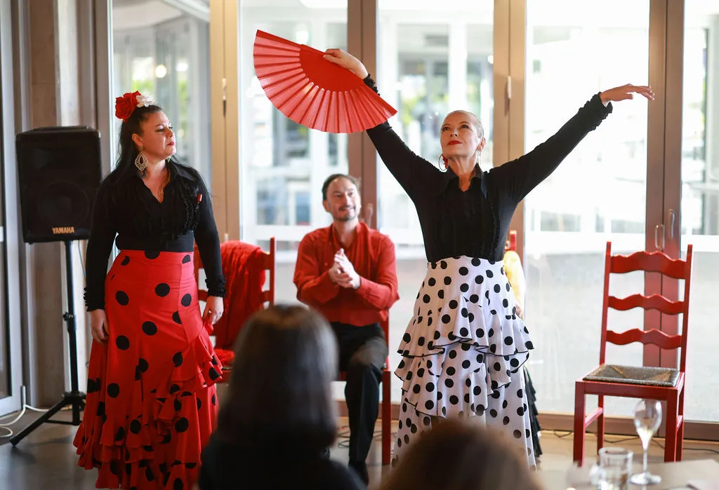 Three Spanish performers - one holding a red fan arms out wide in a dance