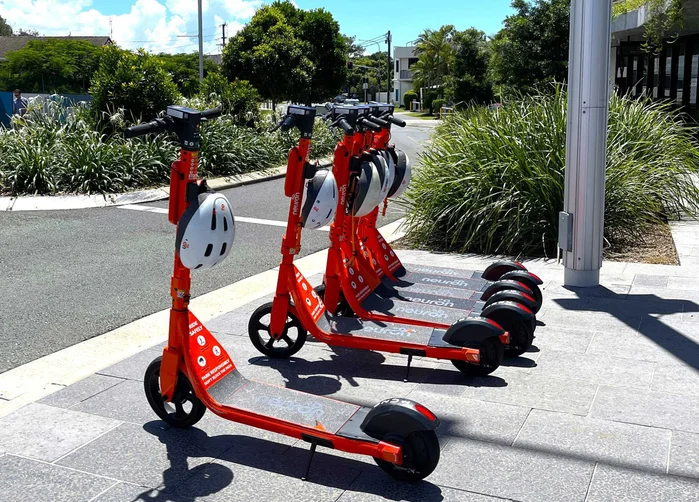 Bright orange electric scooters are lined up on a Maroochydore street corner.