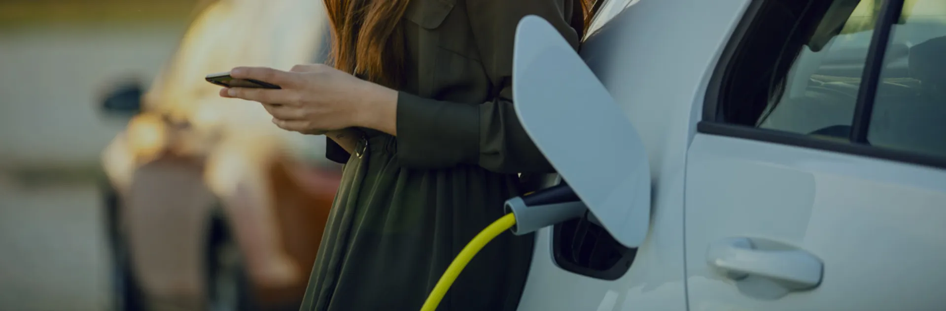 Woman on her phone next to an electric car charging