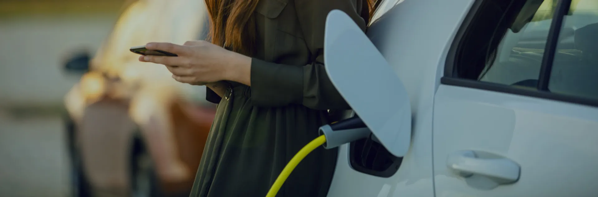 Woman on her phone next to an electric car charging.